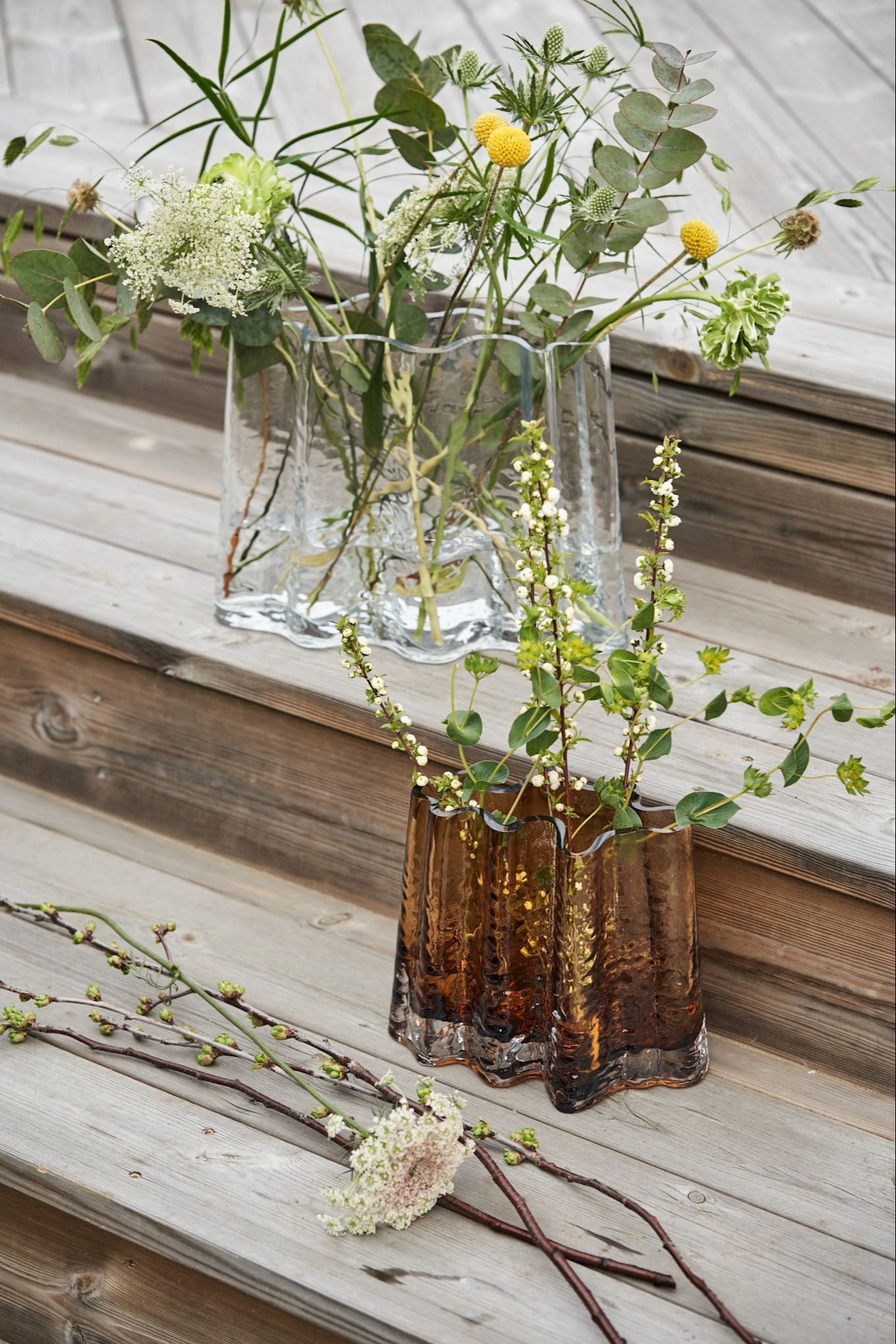 Gry-vasen i klar og cognac står på et tredekke omgitt av vårblomster.