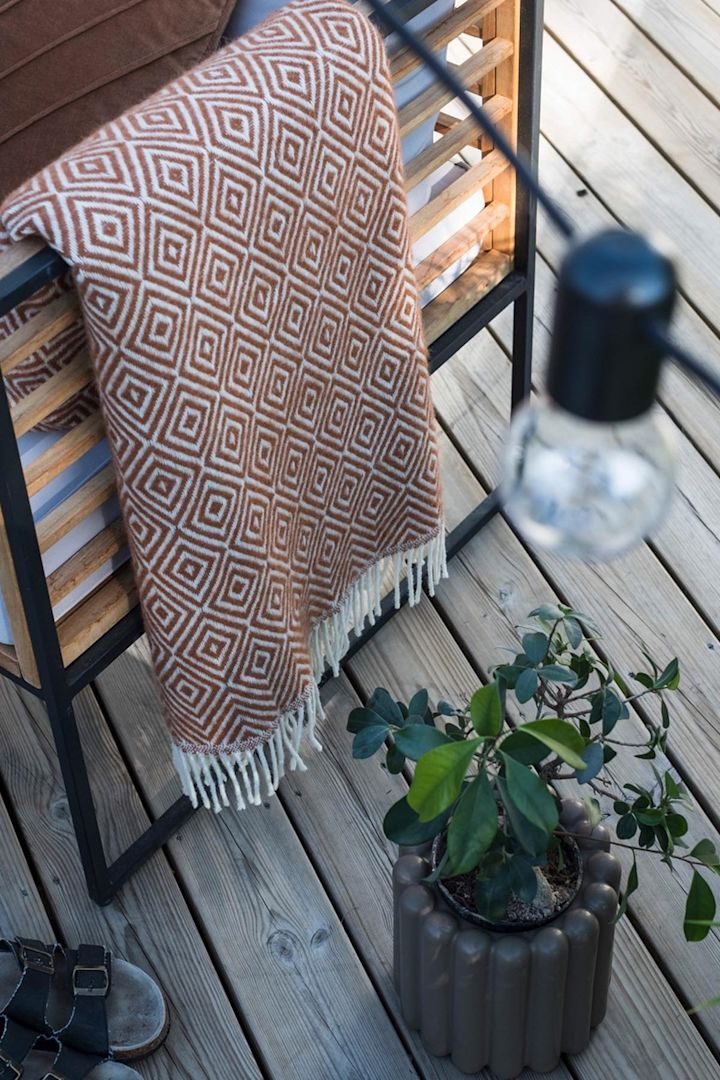 Den brune Mist-blomsterkrukken fra DBKD står på terrassen ved siden av en benk med et pledd hjemme hos @lindaz.se.