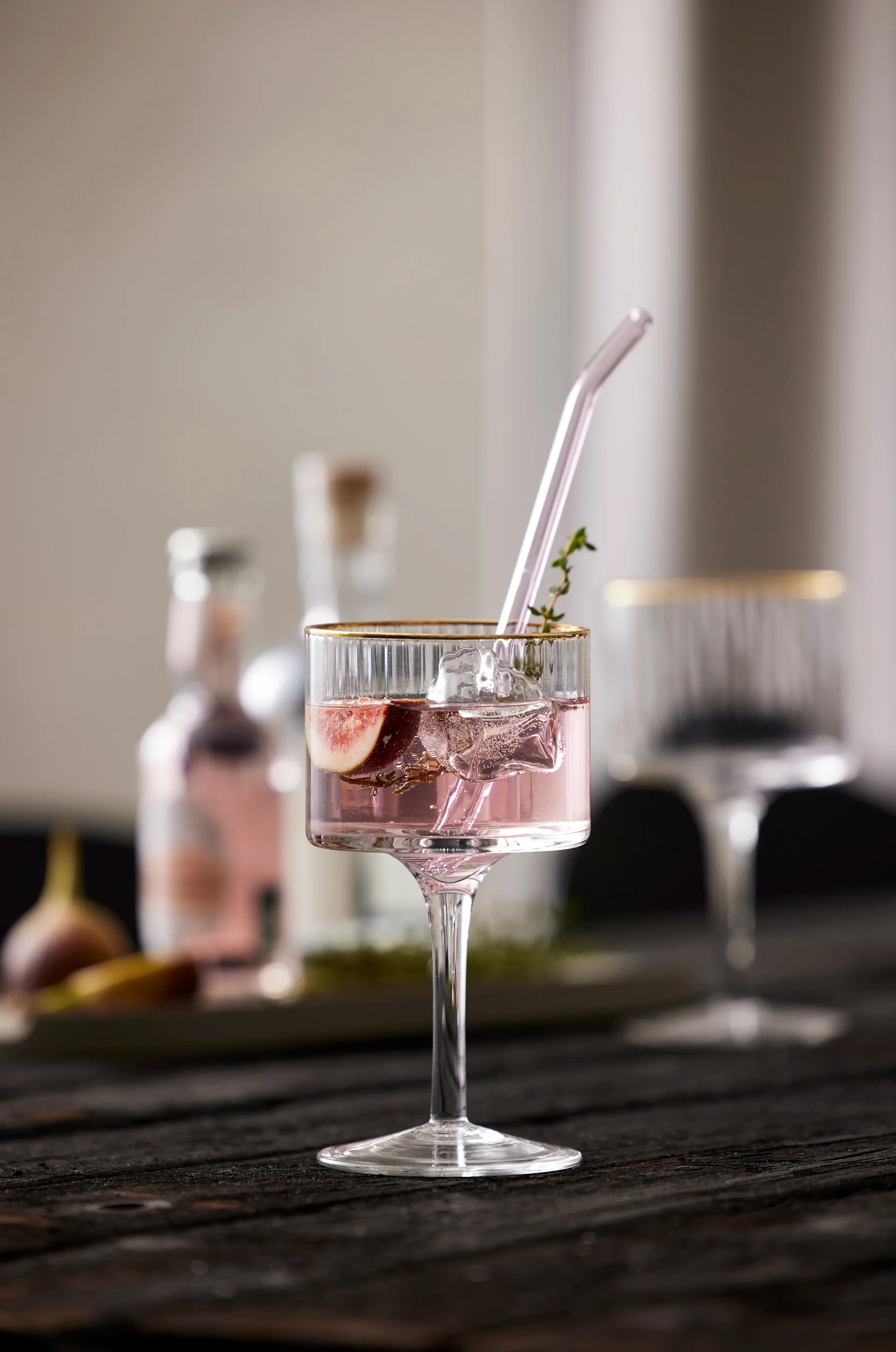 En lilla mocktail med glassugerør og timianpynt står på et bord, servert i et Palermo Gold Gin & Tonic-glass fra Lyngby Glas.