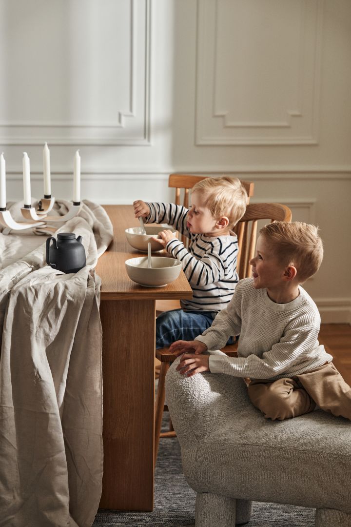 To gutter sitter ved et middagsbord fra Design House Stockholm, bildet viser også Lulu-puff og skåler fra NM&Sand-serien.