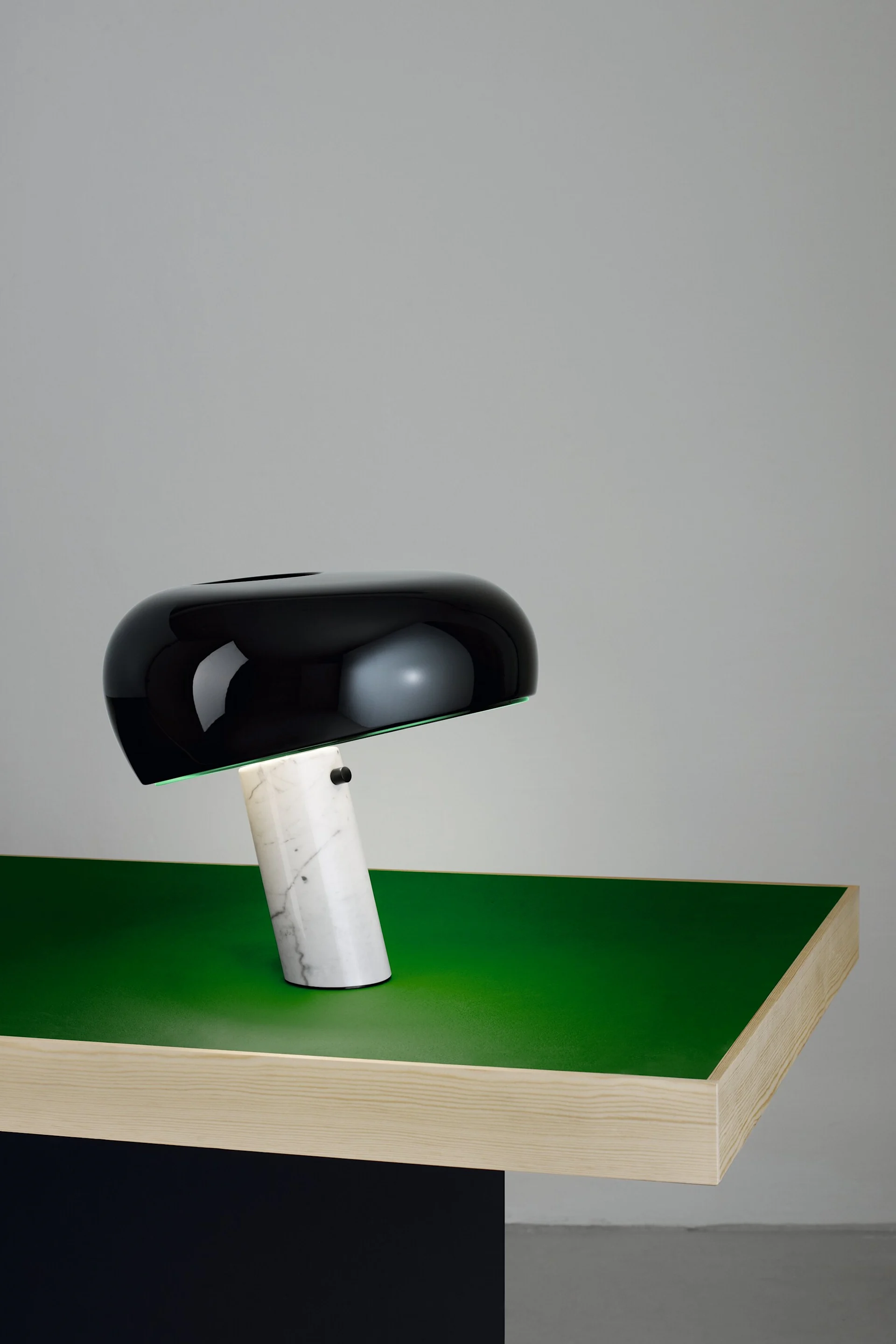 En svart Snoopy-bordlampe fra Flos med marmorfot står på et stilrent, grønt bord. Lampen er en klassisk designlampe.
