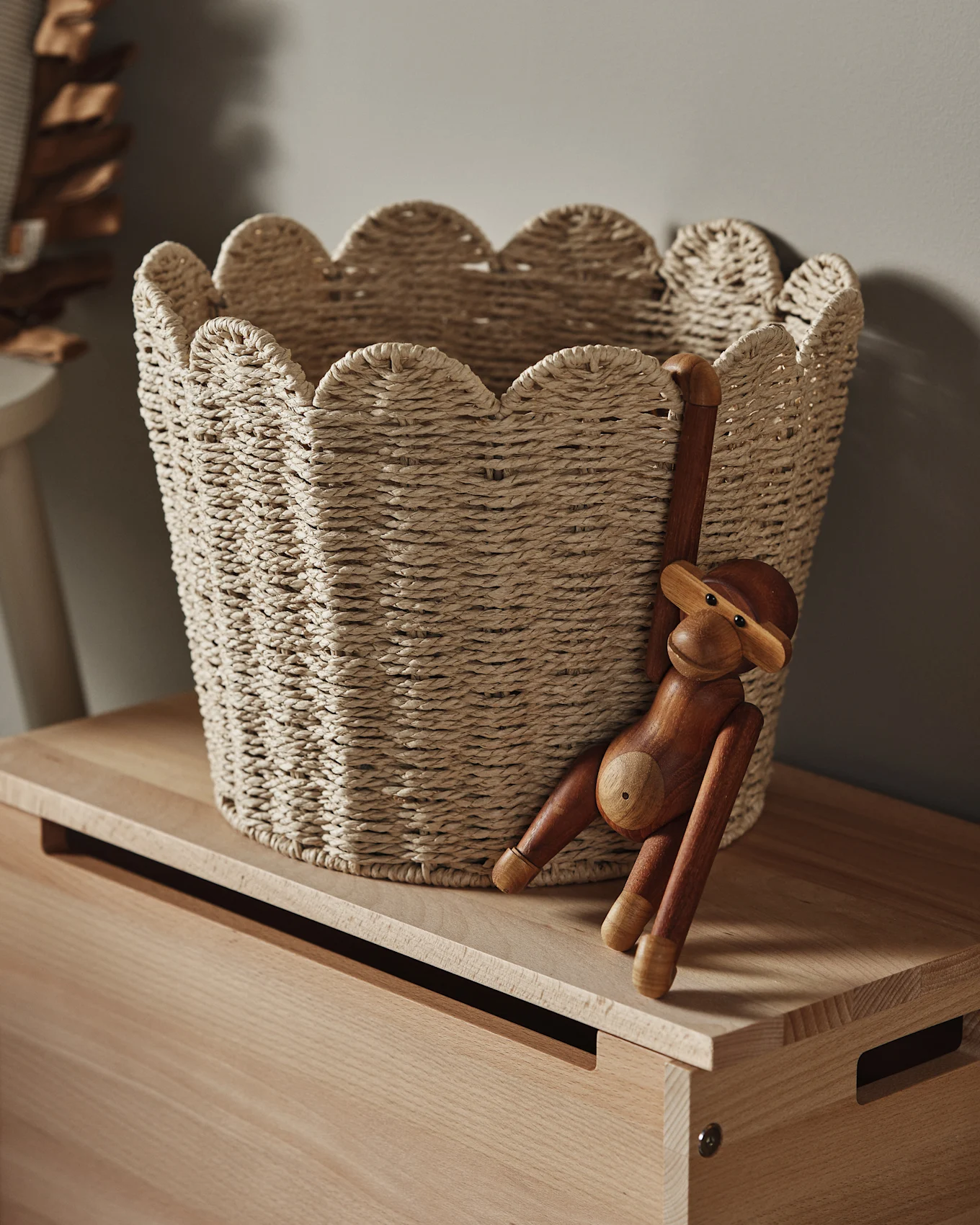 En lys flettet kurv med bølget kant står på en treoverflate, med en treapefigur hengende fra siden.