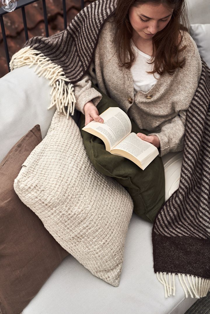 En kvinne sitter i en sofa på balkongen og leser en bok.