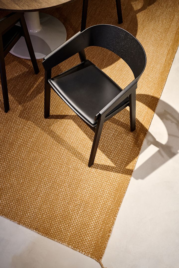 Den svarte Cover-lenestolen med skinnsete fra Muuto står på et sennepsfarget teppe.