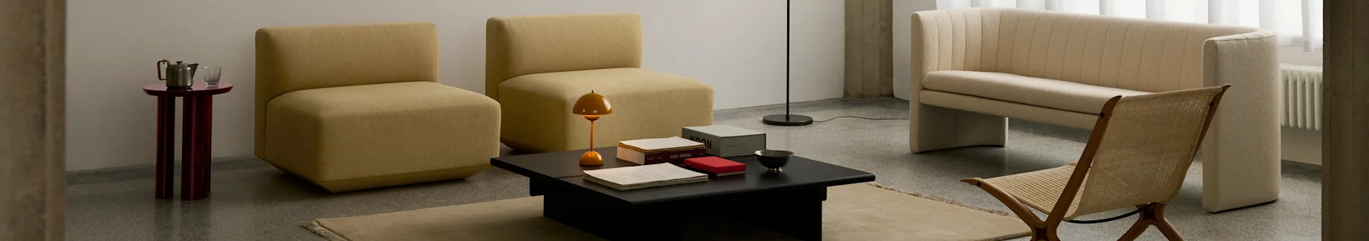 Et moderne stue med to sennepsgule armløse stoler, et svart sofabord, en kremfarget ribbet sofa og en flettet trestol.