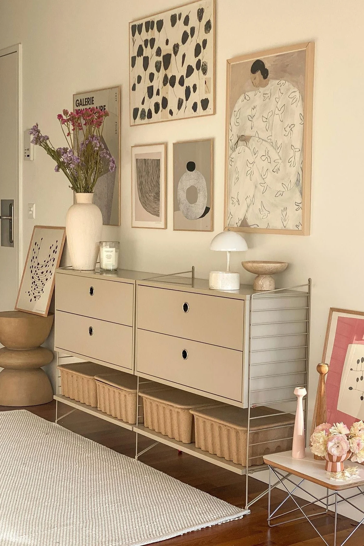 Et moderne rom med et beige modulskap, skuffer og oppbevaringskurver. En vase med blomster, lampe og abstrakt kunst pryder rommet.