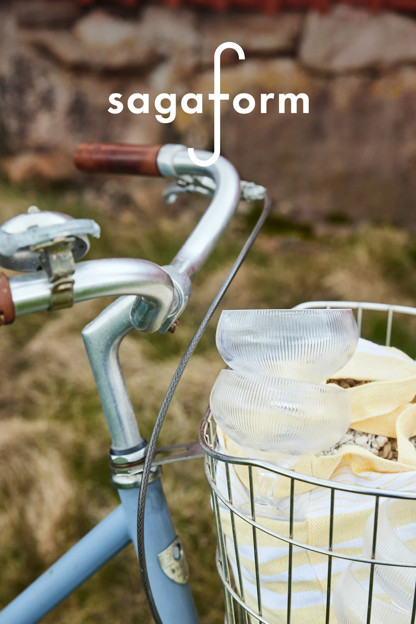 To klare, riflede glassboller og et gulstripet håndkle i en sykkelkurv. 'sagaform'-logo.