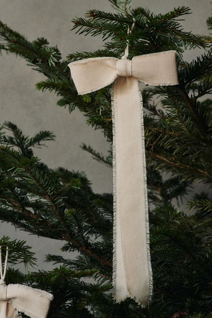 En Bow-dekorasjonsanhenger i sløyfeform fra Ferm Living henger på et juletre.
