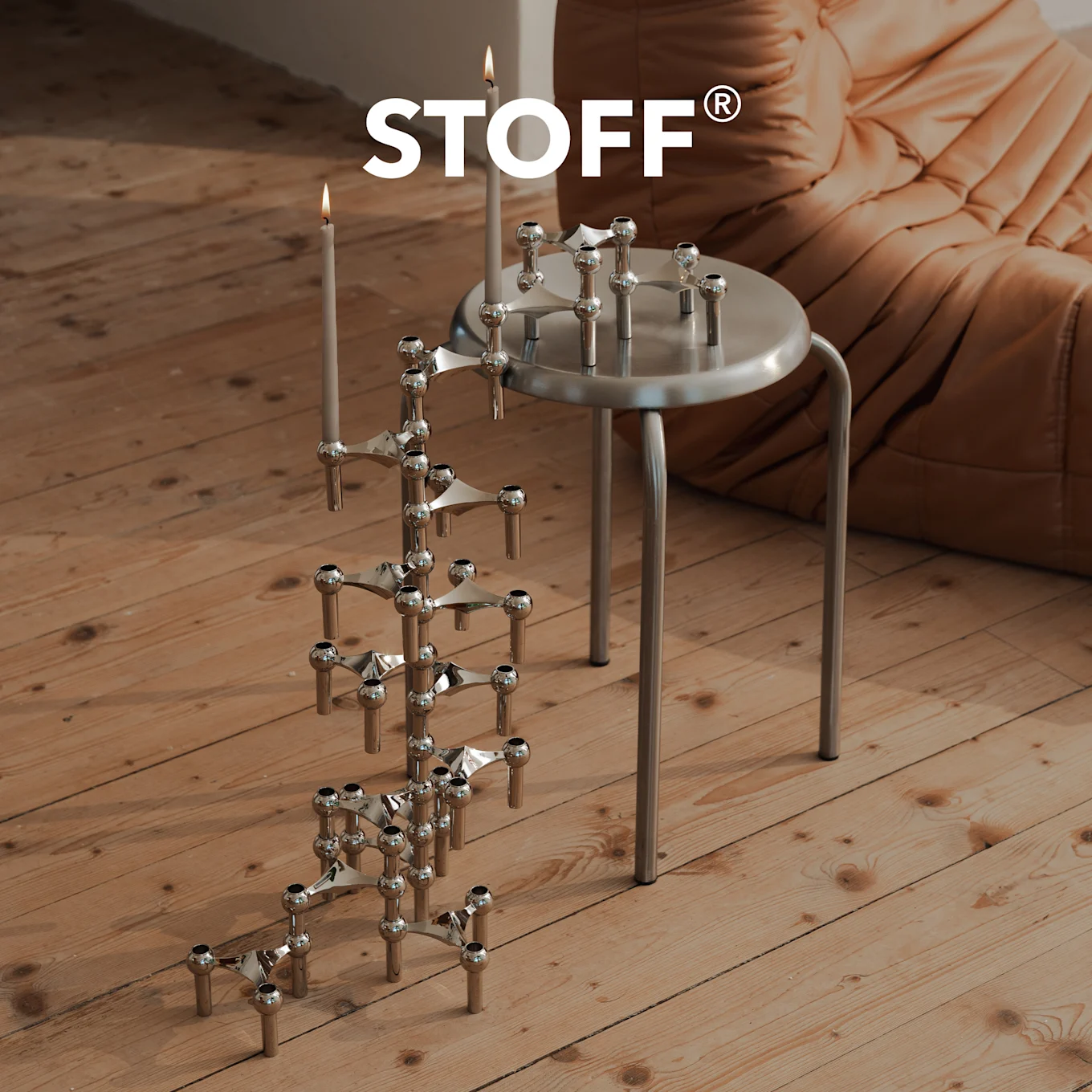 STOFF-logo over krom lysestake med tente lys på tregulv, og en annen på en sølvtaburett.