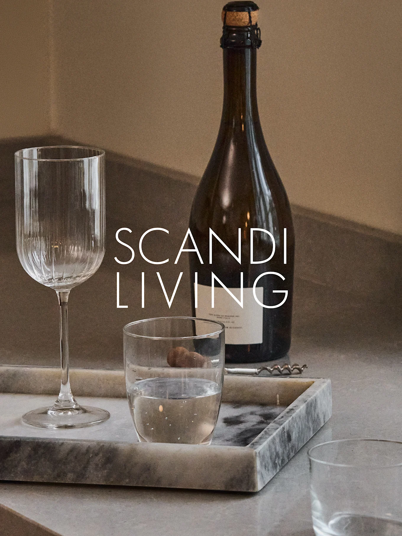 En mørk flaske, et ribbet vinglass, et vannglass og en korketrekker på et marmorbrett med teksten 'SCANDI LIVING'.
