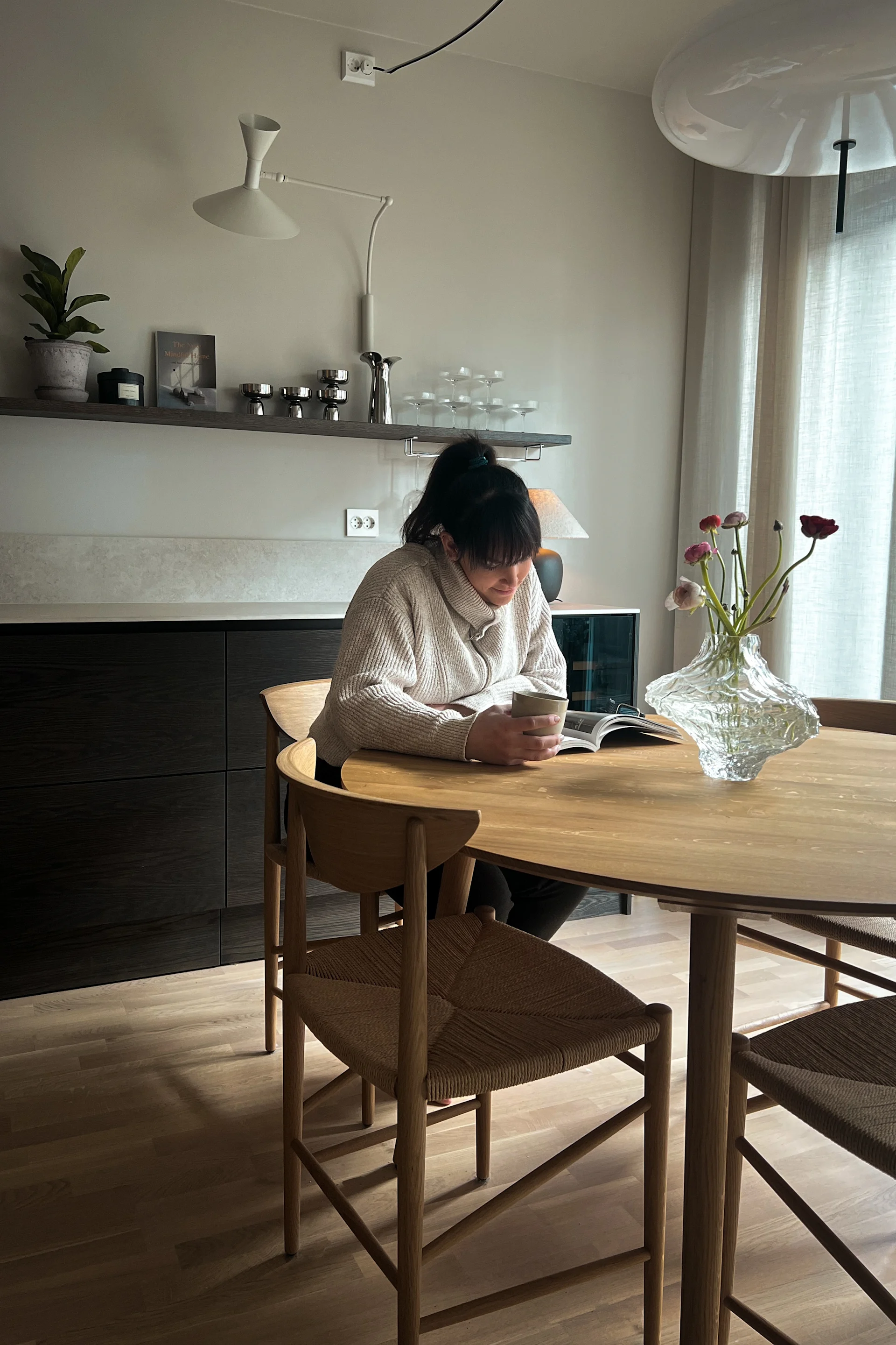 Influenser Helene Wold @villanyhus leser avis på &Tradition spisegruppe i lyst tre med statementvase fylt med blomster foran.