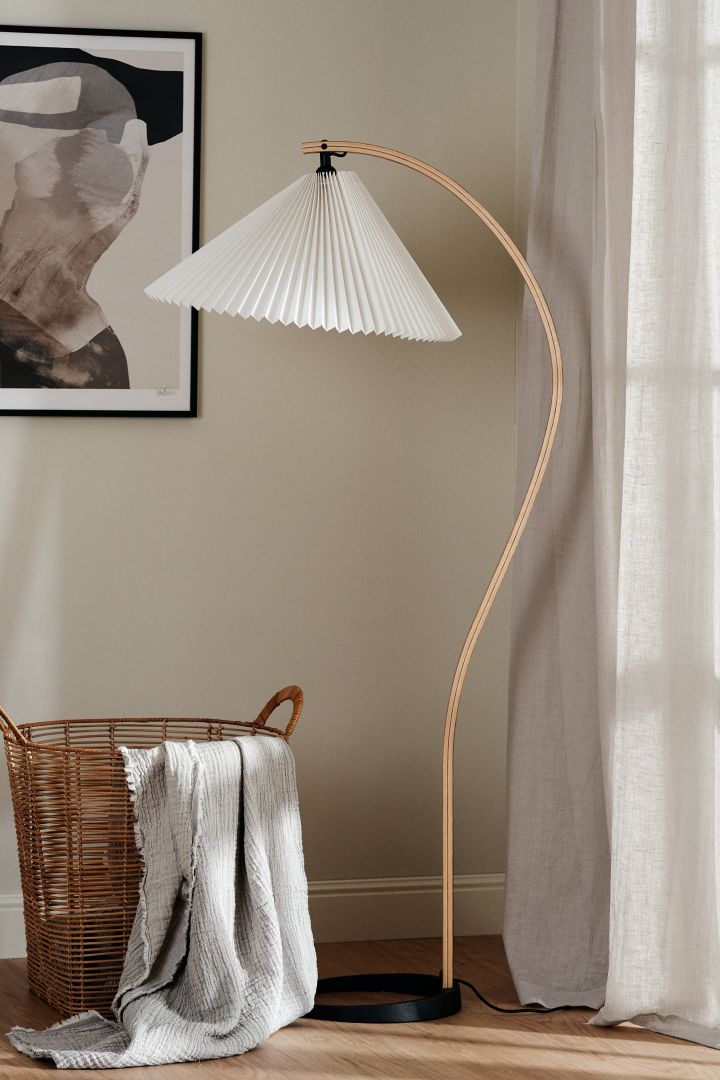 Timberline gulvlampen fra Gubi er et tips for en trendy lampe med plissert lampeskjerm, den har en buet trearm i eik og er perfekt å ha i stua.