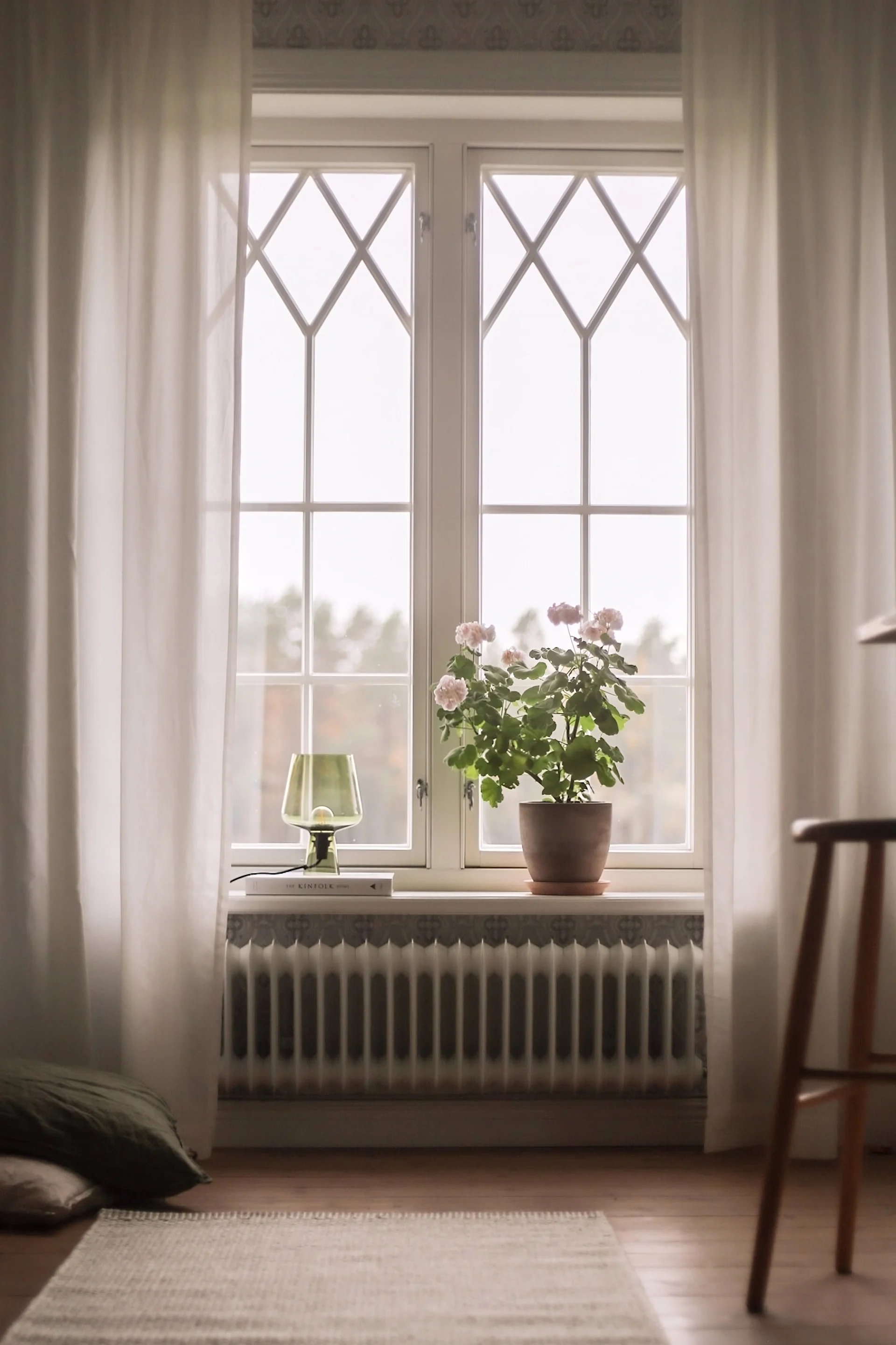 Pynt vinduskarmen med en potteplante og Leimu bordlampe fra Iittala, plassert på en liten bokstabel.
