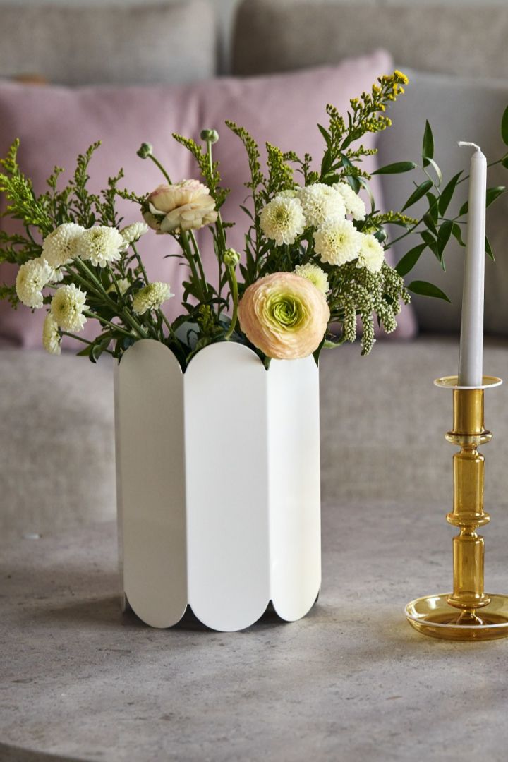 En blomsterbukett i hvit Arcs vase ved siden av Pirouette kopp med fat og Flare lysestaker i gult og rosa fra HAY.