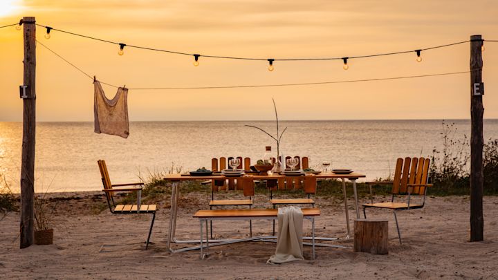 Bli kjent med Grythyttan Stålmöbler, her A2 stoler og A1 bord på stranden ved solnedgang.