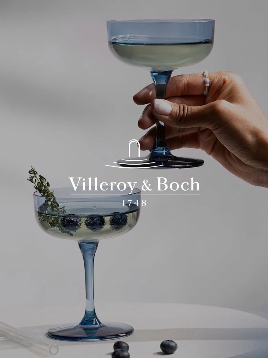 Hånd holder blått coupeglass; et annet glass nedenfor med blåbær, timian og Villeroy & Boch-logo og '1748'.