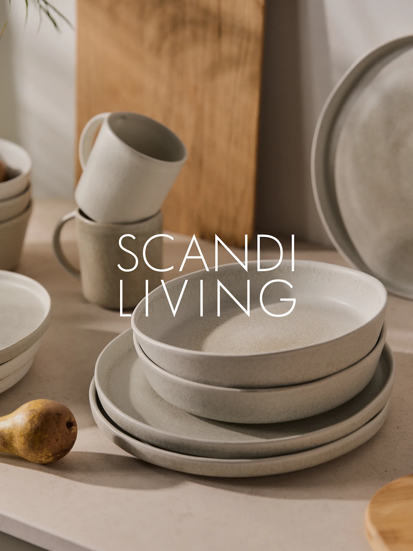 Stabel med lyse, flekkete keramikkfat, skåler og kopper med en pære. Tekst: SCANDI LIVING.