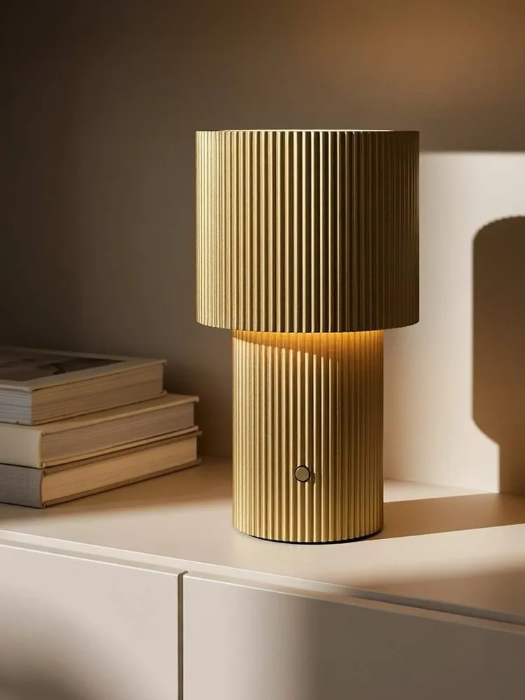 Gullfarget riflet bordlampe, lysende, med en sirkulær knapp på basen.