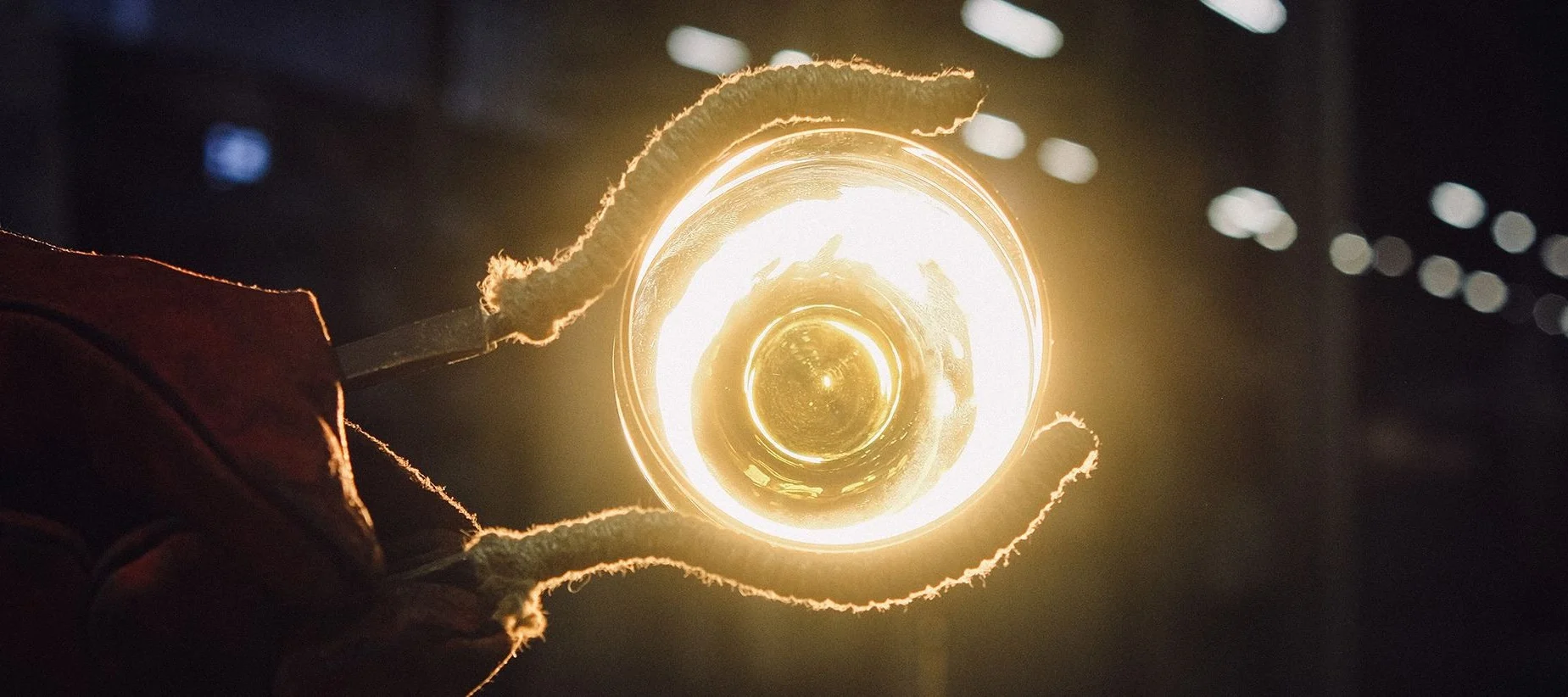 Et par tenger holder opp et glødende glasskunstverk ved Iittala glassverk i Finland.