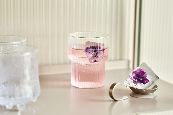 Ripple drikkeglass fra Ferm Living med en rosa drink i og lilla blomst fryst i en isbit.