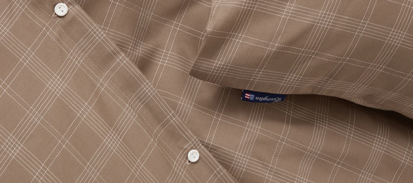 Nærbilde av brunt stoff med hvitt rutemønster, med to hvite knapper og en blå Lexington-etikett.