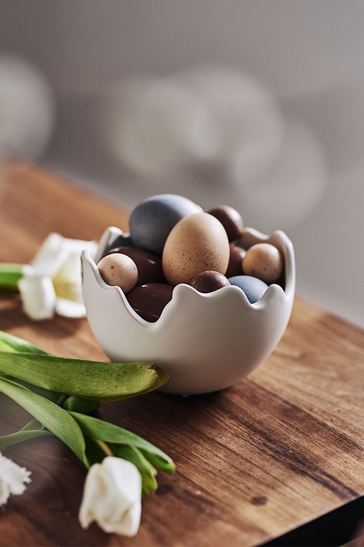Påskepynt: En eggformet skål fra DBKD fylt med fargede egg, naturlige egg og godteriegg – en perfekt kombinasjon av dekor og påskens søte fristelser!