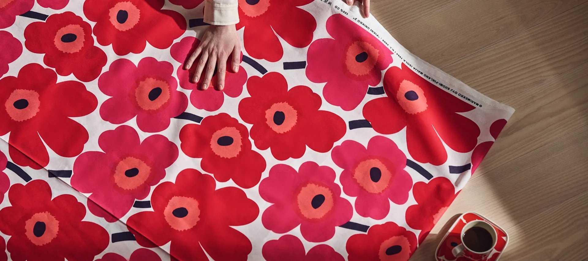 En hånd hviler på et knallrødt Unikko-stoff fra Marimekko.