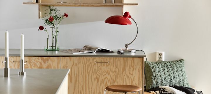 Kaiser Idell lampe i rødt, Ikaru vase og design fra Fritz Hansen i et stilrent, moderne kjøkken med kryssfiner. 