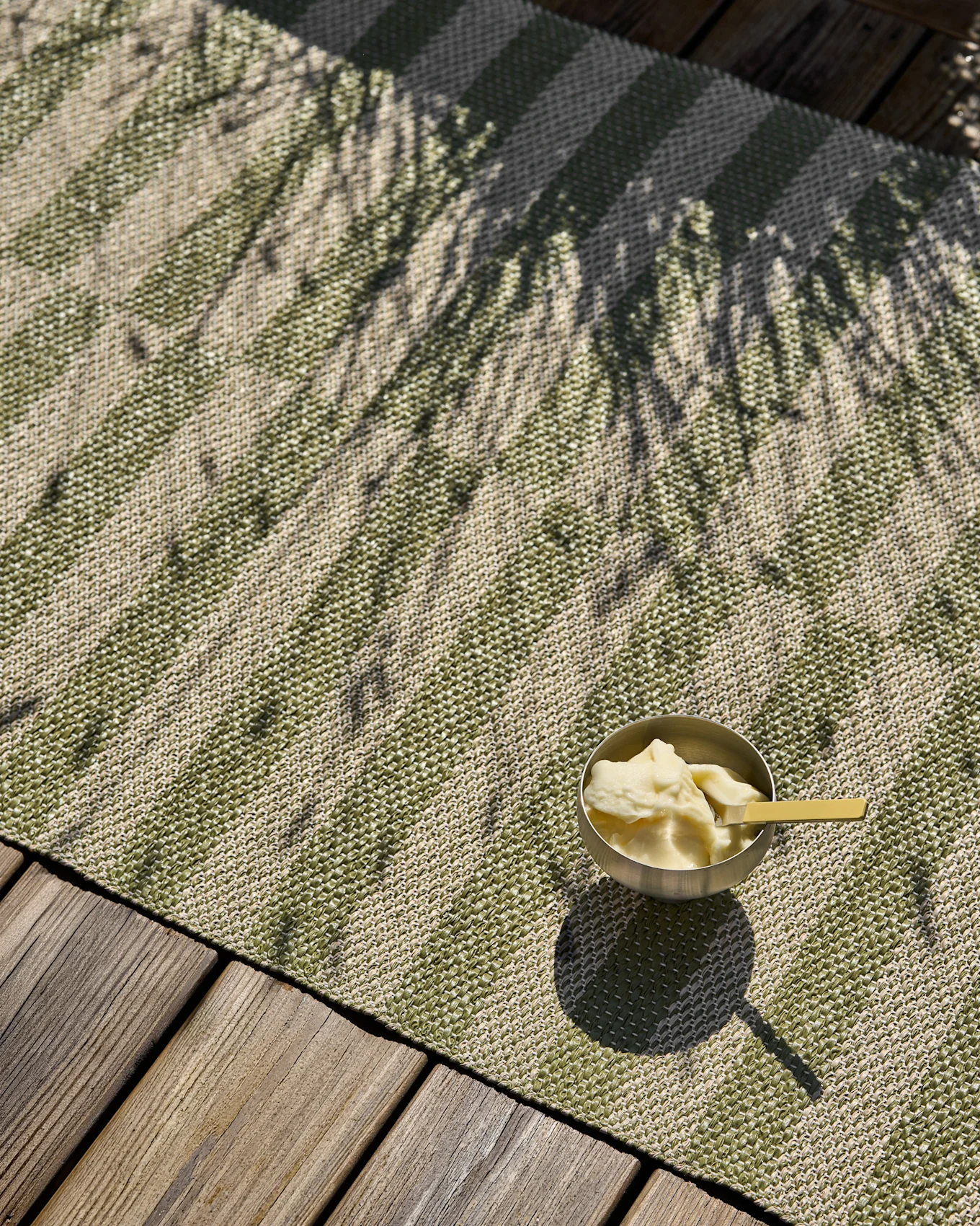 Grønt og beige stripete vevd teppe med en bolle is og palmskygger på en treterrasse.