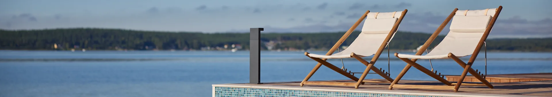 To hvite stoff- og tredekksstoler på en terrasse med utsikt over en innsjø og en skog i det fjerne.
