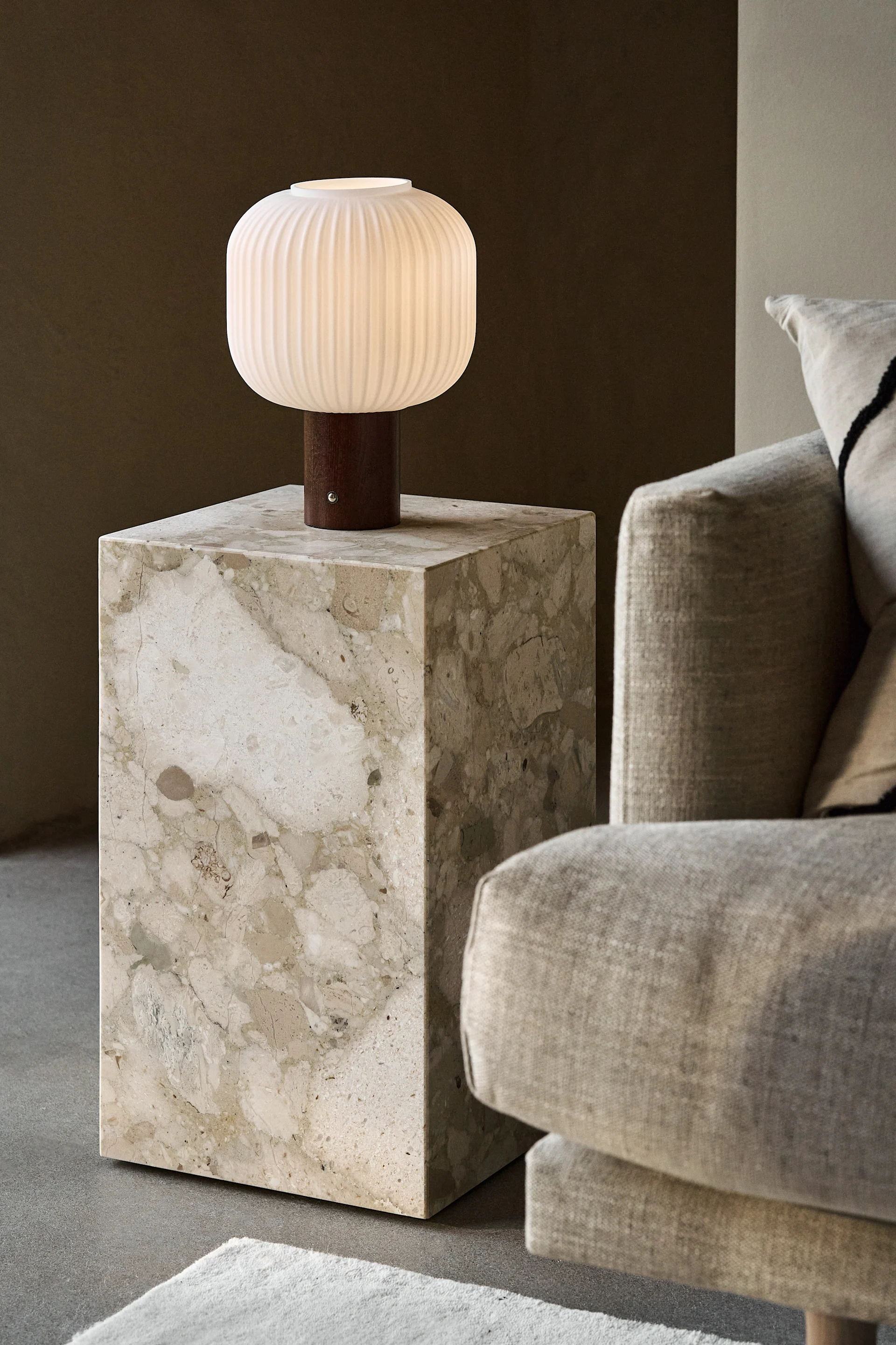 En tent, riflet, hvit bordlampe med trebunn på et beige marmorbord ved siden av en lys sofa.