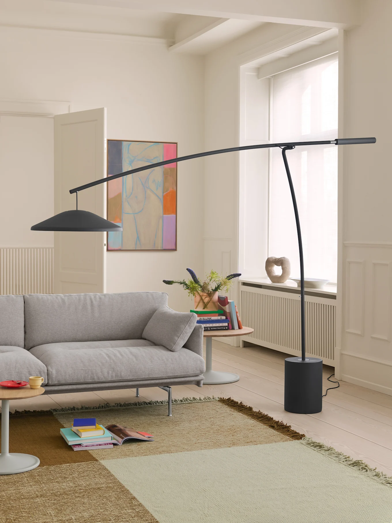 En moderne stue med lysegrå sofa, høy mørkegrå buet gulvlampe og et mønstret teppe på lyst tregulv.