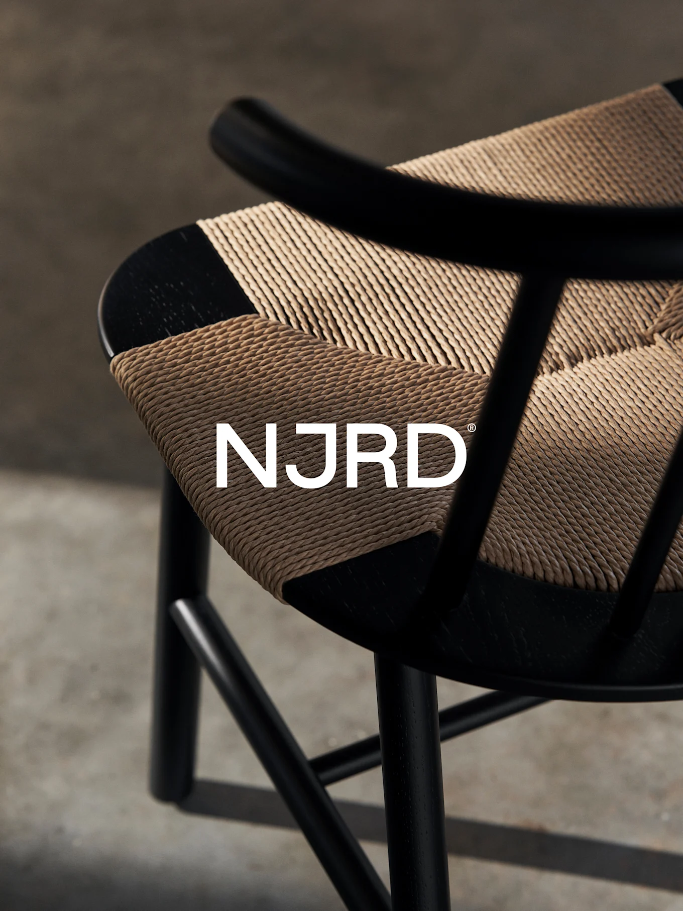 Nærbilde av en svart stol med et vevd lysebrunt sete, med den hvite 'NJRD'-logoen.