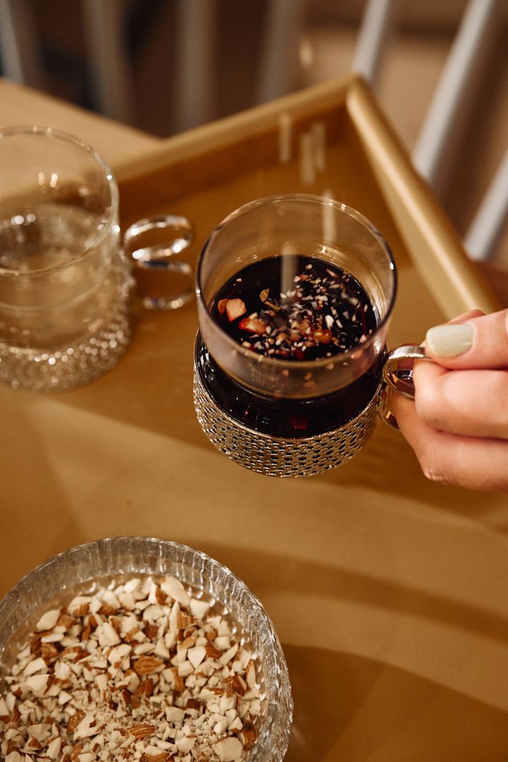 Noen drysser mandler i et glass fylt med gløgg.