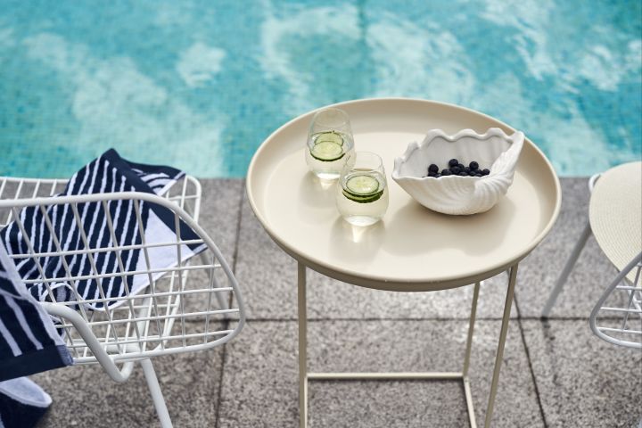 Et beige salongbord fra Norr11 er en sommerfavoritt denne sommeren, på bordet står et Scandi Living vannglass med agurkskiver i sammen med en Shell-skål fra By On fylt med blåbær. 