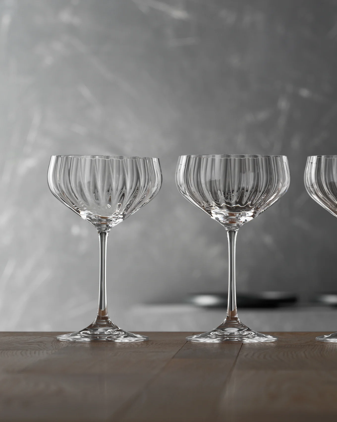 Tre tomme, klare riflede champagneglass på et trebord mot en grå bakgrunn.