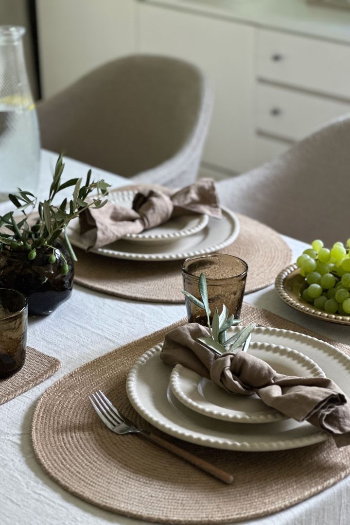 En elegant grå borddekking med Swedish Grace-serviset i fargen Dimma, elegant bestikk fra Scandi Living og grønn plante som en bordløper på bordet.
