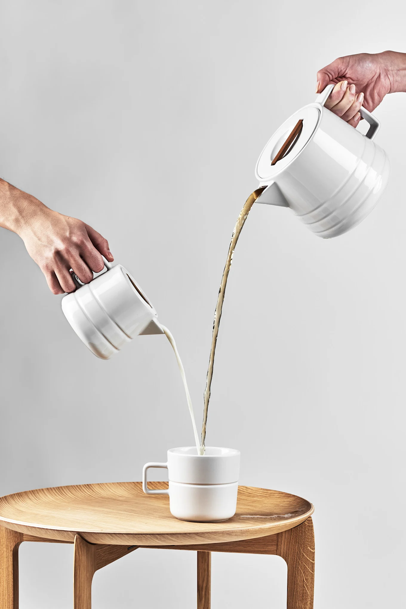 Store kaffekopper: Den hvite Lines-koppen fra NJRD står på et sidebord, mens kaffe og melk helles i fra hver sin kanne ovenfra.
