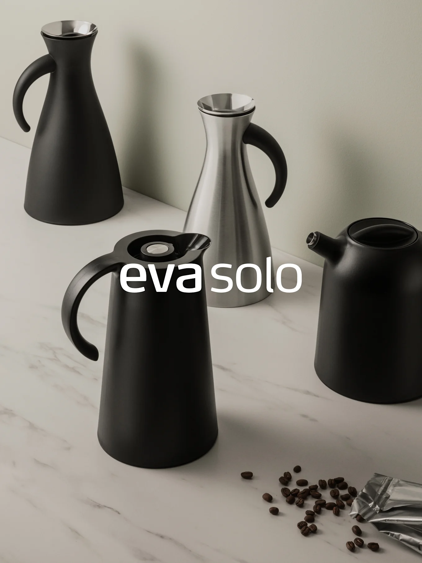 Fire svarte/sølv karafler og en svart vannkoker på marmor med kaffebønner og foliepakke.