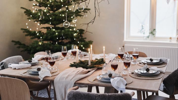 En hvit og minimalistisk borddekking til jul til årets julemiddag, med naturlige dekorasjoner som kongler og granbar på bordet.