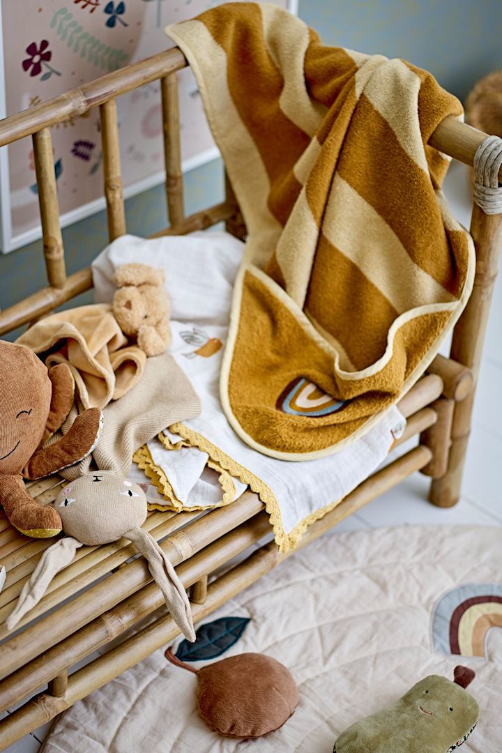 Et gult og brunt badehåndkle med hette og regnbue-motiv henger over armen på en benk sammen med en blekksprut-leke, en ideell gave til babyshower