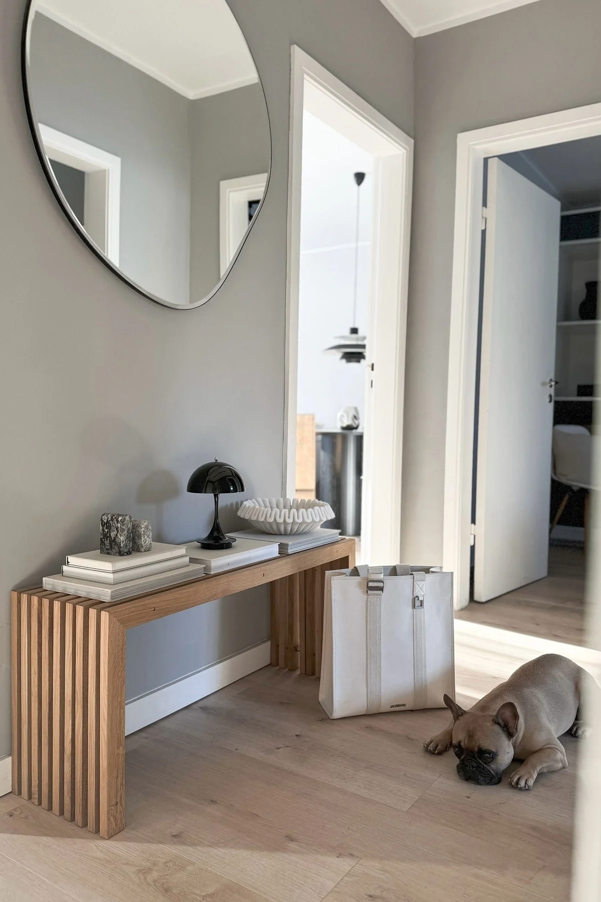 Den helhetlig utformede entréen til @alexander.stoeckel, med Pond Mirror fra Ferm Living, Panthella-bordlampen på en benk og en hund.
