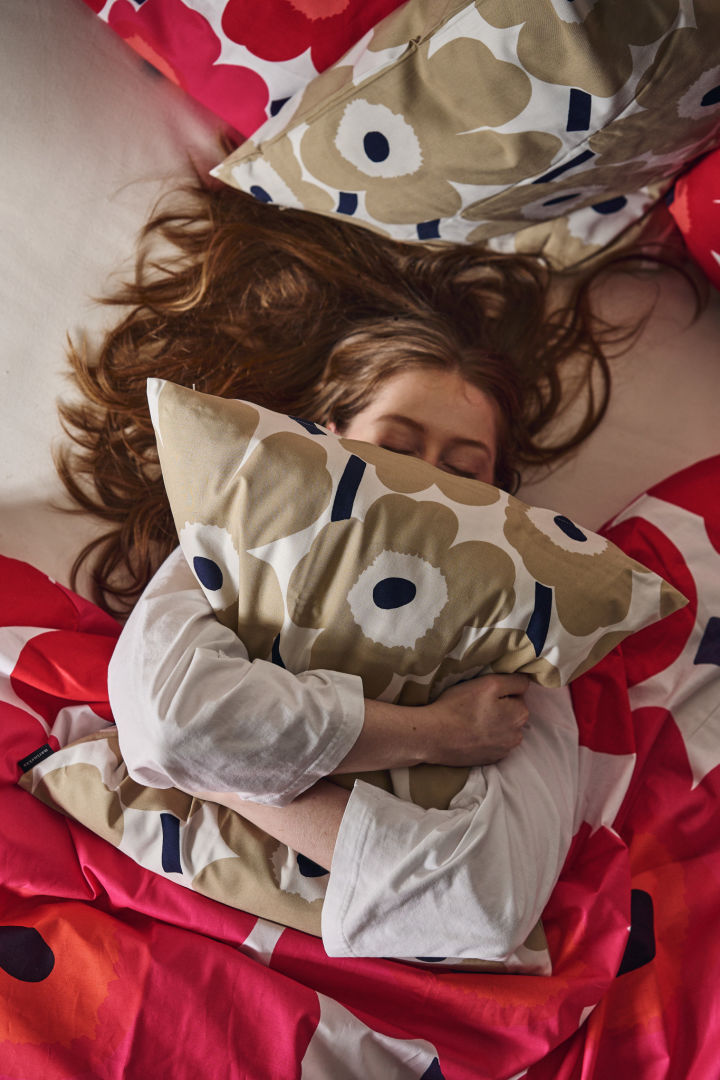 En kvinne klemmer Unikko-puten i sengen omgitt av Unikko-sengetøy i rødt og rosa.