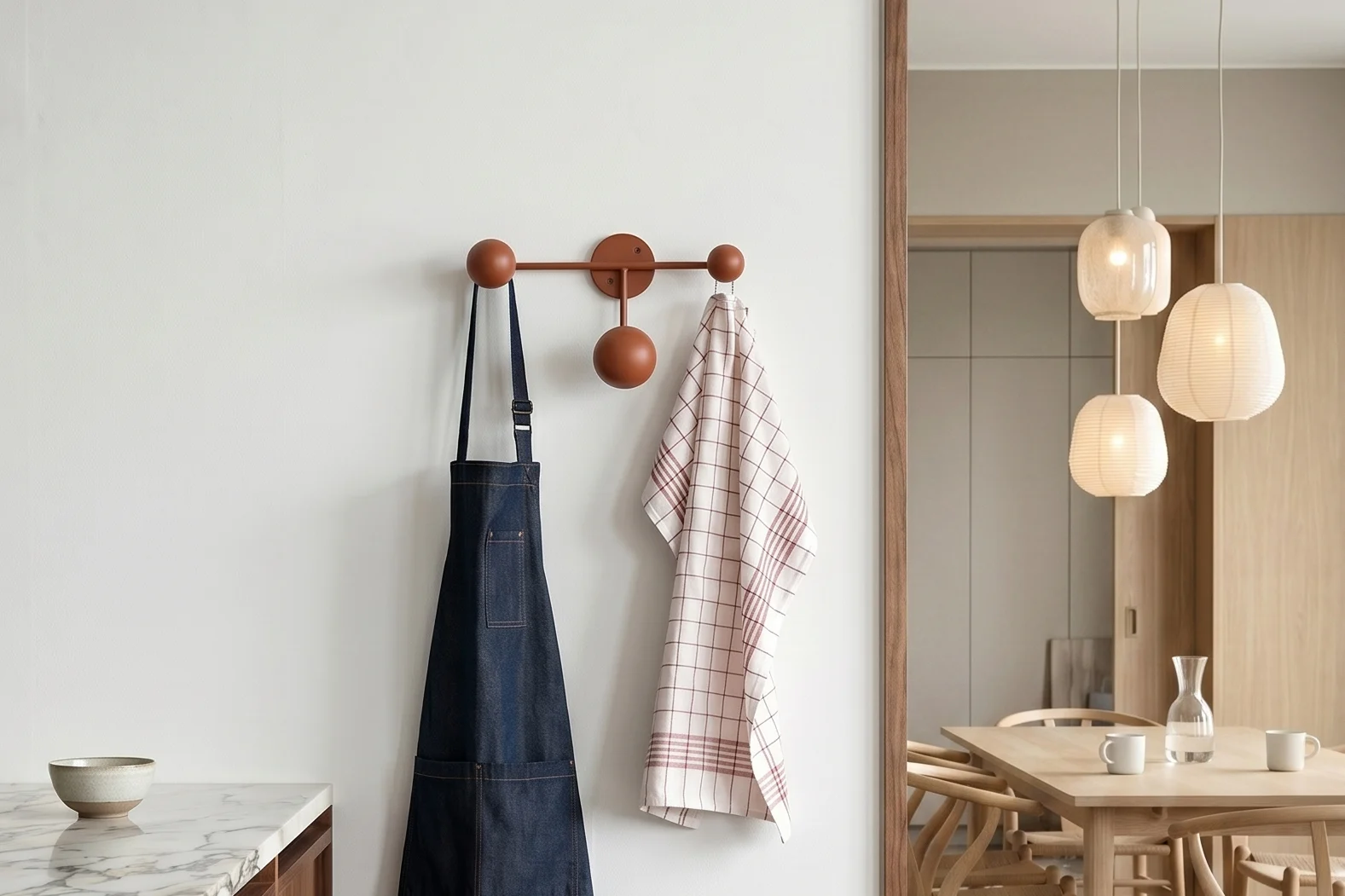 Kjøkken med marmor. Blått forkle, rutete håndkle på knaggrekke. Spisestue med bord og pendellamper.