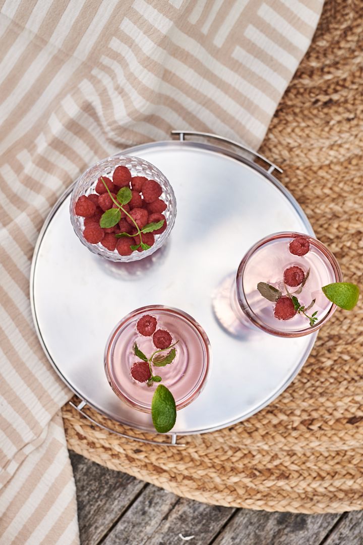 Et praktisk brett er et bra shoppingtips for sommeren slik at du enkelt kan servere drinker eller desserter på det. Her et brett i stål fra Stelton med rosa drinker på. 