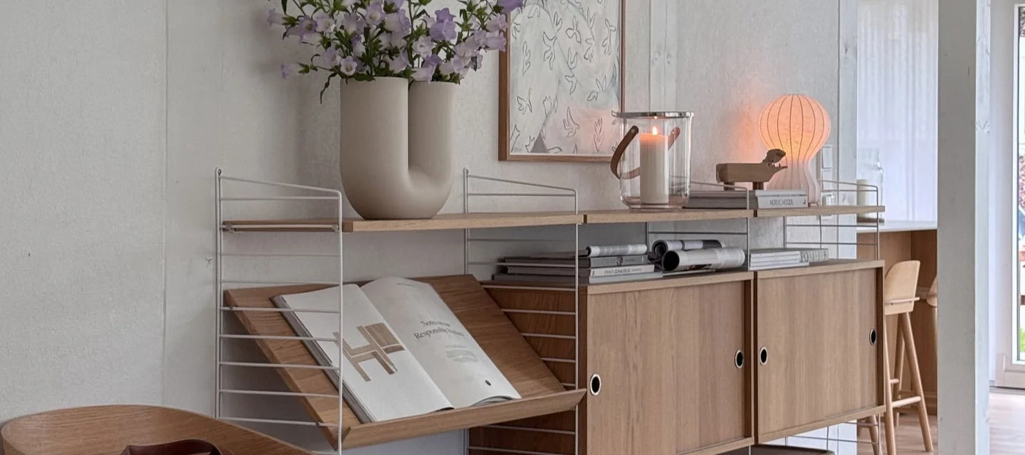 Modulært hyllesystem med hvite rammer, trehyller, skap, vase med blomster, lykt og glødende sopplampe.