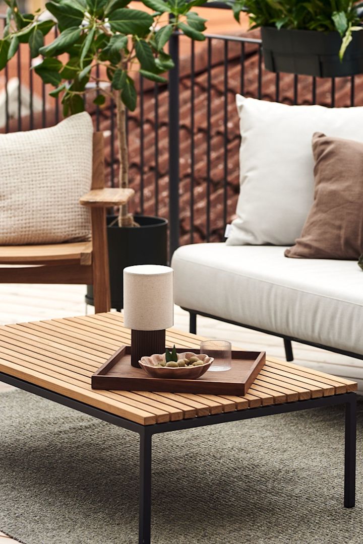 Den bærbare og oppladbare lampen Manhattan fra &tradition er perfekt å dekorere uteplassen med som her på et enkelt sofabord i tre.
