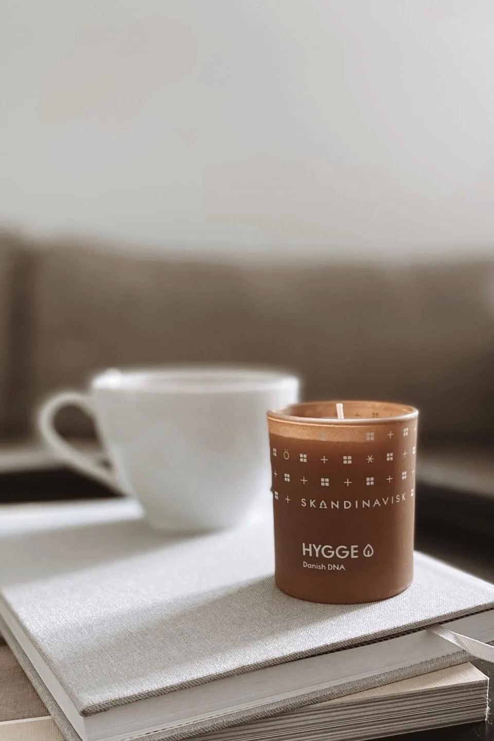 Et duftlys som Hygge-lyset fra Skandinavisk, som her står på en bokstabel på et sofabord, er en fin gave til valentinsdag for koselige kvelder.