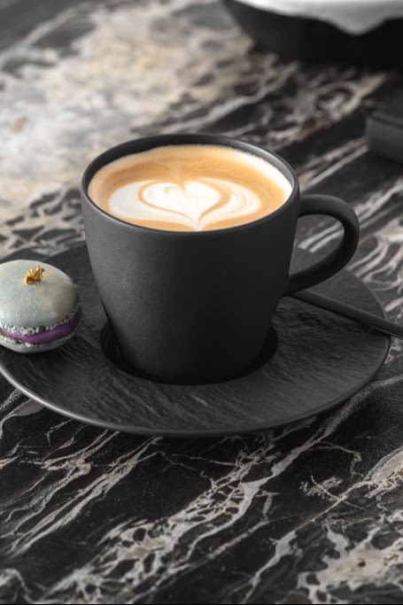 En svart kaffekopp med melkeskumkunst på toppen.