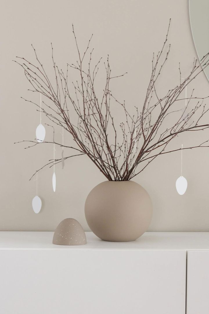 Påskepynt: En påskeriskvist står også på en hvit kommode i en sandfarget kulevase med påskeheng i eggform, begge fra Cooee Design, hjemme hos @tunadalens. 